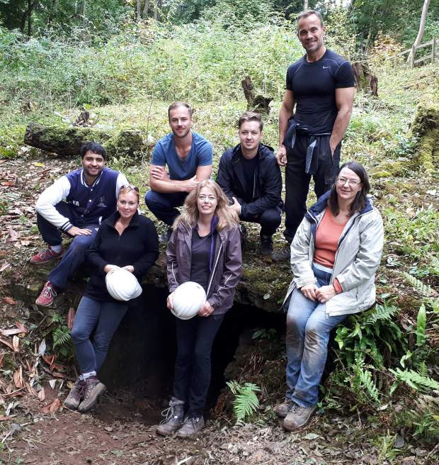 The team pose for a photo outside, sitting and standing on a large fallen tree.